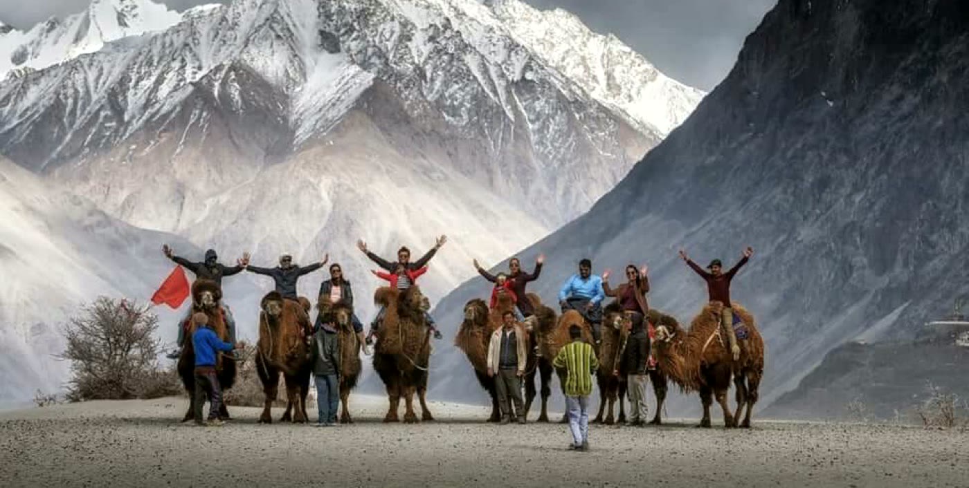 Bactrian camels and travellers on the high desert floor of Nubra Valley, Ladakh, beneath snow peaks